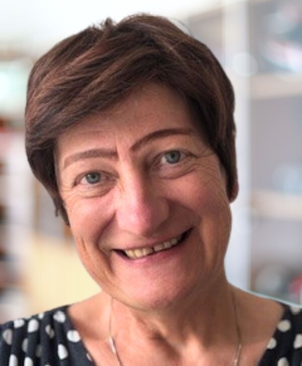 Bild vergr&ouml;&szlig;ern: Portr&auml;t einer l&auml;chelnden Frau mit kurzen braunen Haaren und blauen Augen, die ein dunkelblaues Oberteil mit wei&szlig;en Punkten tr&auml;gt.