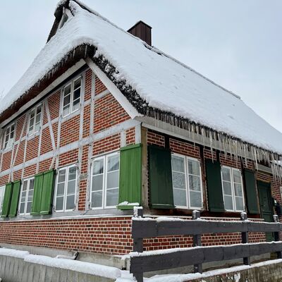 Bild vergr&ouml;&szlig;ern: Fachwerkhaus mit gr&uuml;n lackierten Fensterl&auml;den und schneebedecktem Dach, an dem lange Eiszapfen h&auml;ngen
