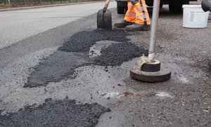 Bild vergr&ouml;&szlig;ern: Ein Mann arbeitet an einer Stra&szlig;e mit Kaltasphalt, der mit Gewichten verdichtet wird.