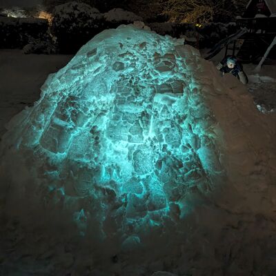 Bild vergr&ouml;&szlig;ern: Symbolbild zum Winter - Leuchtendes Iglu aus Schnee bei Nacht mit blau-gr&uuml;nem Licht von innen