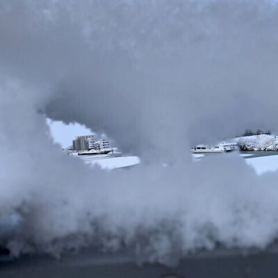 Bild vergr&ouml;&szlig;ern: Symbolbild zum Winter - Schneel&ouml;cher in einer Schneedecke mit Blick auf schneebedeckte Geb&auml;ude im Hintergrund