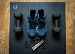 Symbolbild f&uuml;r einen Sportkurs - Zwei blaue Sportschuhe, zwei Hanteln und ein Springseil auf dunklem Untergrund angeordnet