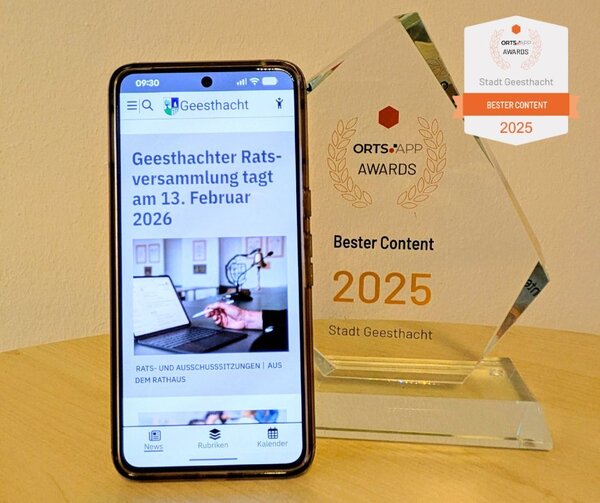 Smartphone mit der GeesthachtApp auf dem Bildschirm neben einem gl&auml;sernen Orts.App-Award mit der Aufschrift 'Bester Content 2025 Stadt Geesthacht'