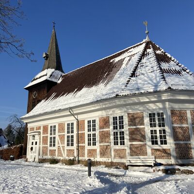 Bild vergr&ouml;&szlig;ern: Schneebedeckte Landschaft mit verschneiter Kirche im Hintergrund.