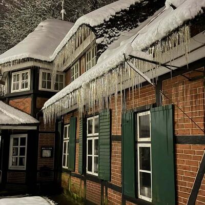 Bild vergr&ouml;&szlig;ern: Eiszapfen bilden sich unter dem Dach eines Geb&auml;udes, w&auml;hrend Schnee den Boden bedeckt.