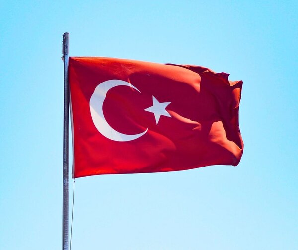 Die Nationalflagge der T&uuml;rkei weht an einem silbernen Mast vor einem strahlend blauen, wolkenlosen Himmel. Das rote Flaggentuch zeigt zentral einen wei&szlig;en Halbmond und einen wei&szlig;en, f&uuml;nfzackigen Stern.