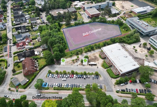 Luftaufnahme eines Schulgel&auml;ndes am D&uuml;sselbuschberg mit eingezeichneten Markierungen f&uuml;r ein Verkehrskonzept. Eine gro&szlig;e, r&ouml;tlich schraffierte Fl&auml;che im Zentrum ist als &raquo;BvS-Container&laquo; markiert. Im Vordergrund befindet sich ein Parkplatz mit zwei Bushaltestellen-Symbolen. Ein Pfeil am linken Rand weist auf den &raquo;Schulweg&laquo; hin, der in ein angrenzendes Wohngebiet f&uuml;hrt.