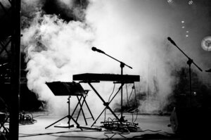 Ein Schwarz-Wei&szlig;-Foto einer dunklen B&uuml;hne. In der Mitte steht ein Keyboard mit einem Mikrofon. Links daneben steht ein Notenst&auml;nder. Dichter B&uuml;hnenrauch h&uuml;llt den Hintergrund ein.