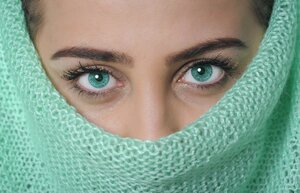 Eine nahr&auml;umliche Aufnahme zweier Frauen an einem Tisch im Rahmen einer Farb- oder Typberatung. Die linke Frau mit Brille und kurzen Haaren h&auml;lt konzentriert ein gro&szlig;es, leuchtend orangefarbenes Tuch direkt unter das Kinn der rechten Frau, um die Wirkung der Farbe auf deren Hautton zu pr&uuml;fen. Die beratene Frau hat mittellanges, hellbraunes Haar, schaut aufmerksam nach vorne und tr&auml;gt ein dezentes, dunkles Oberteil. Auf dem hellen Holztisch im Vordergrund liegen weitere farbige Stoffmuster und T&uuml;cher (unter anderem in Blau- und Rott&ouml;nen) bereit. Der Hintergrund ist hell und unaufdringlich gehalten.