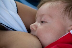 Ein kleines Baby wird gestillt. Es liegt ganz nah an der Brust der Mutter und schaut friedlich zur Seite.