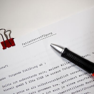 Auf einem wei&szlig;en Dokument steht die &Uuml;berschrift Patientenverf&uuml;gung. Auf dem Papier liegt ein schwarzer Kugelschreiber. Oben links ist eine rote B&uuml;roklammer am Rand festgemacht.
