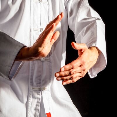 Eine Person in einem wei&szlig;en Kampfsportanzug macht eine ruhige Handbewegung im Stil von Tai-Chi. Zu sehen ist der Oberk&ouml;rper vor schwarzem Hintergrund.