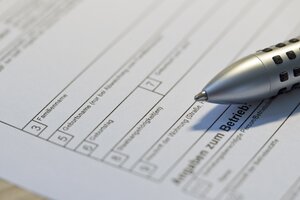 Nahaufnahme eines Formulars auf wei&szlig;em Papier. Zu sehen sind verschiedene Felder zum Ausf&uuml;llen wie Geburtsname und Geburtstag. Die Spitze eines silbernen Kugelschreibers zeigt auf das Papier.