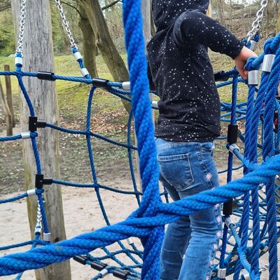 Ein Kind klettert auf einem Spielplatz durch ein Netz aus dicken, blauen Seilen. Es tr&auml;gt einen dunklen Pullover mit kleinen Sternen und eine Jeans.